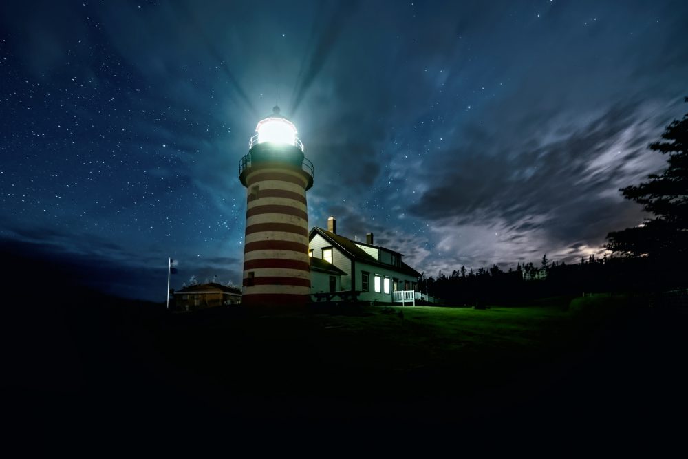 Red and white Striped lighthouse at night. Light shining out into the night sky